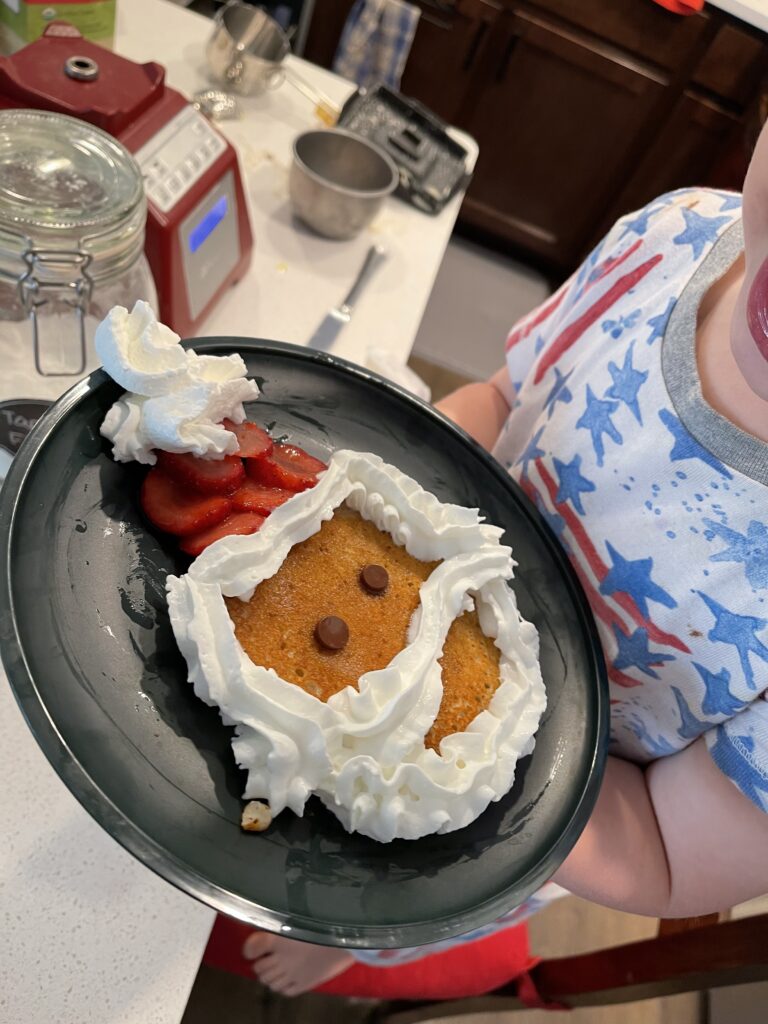 Child holding plate with pancake that looks like a Santa head