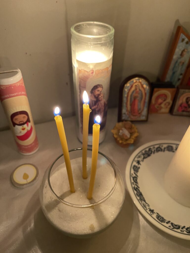 Catholic home altar with 3 thin beeswax candles sitting in sand, large St. Joseph candle, showing how to do liturgical living in the home