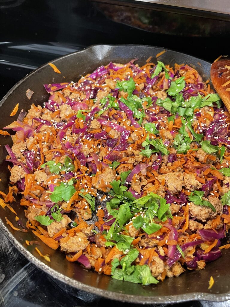 cast iron skillet with Asian food: ground pork, red cabbage, carrots, cilantro, sesame seeds